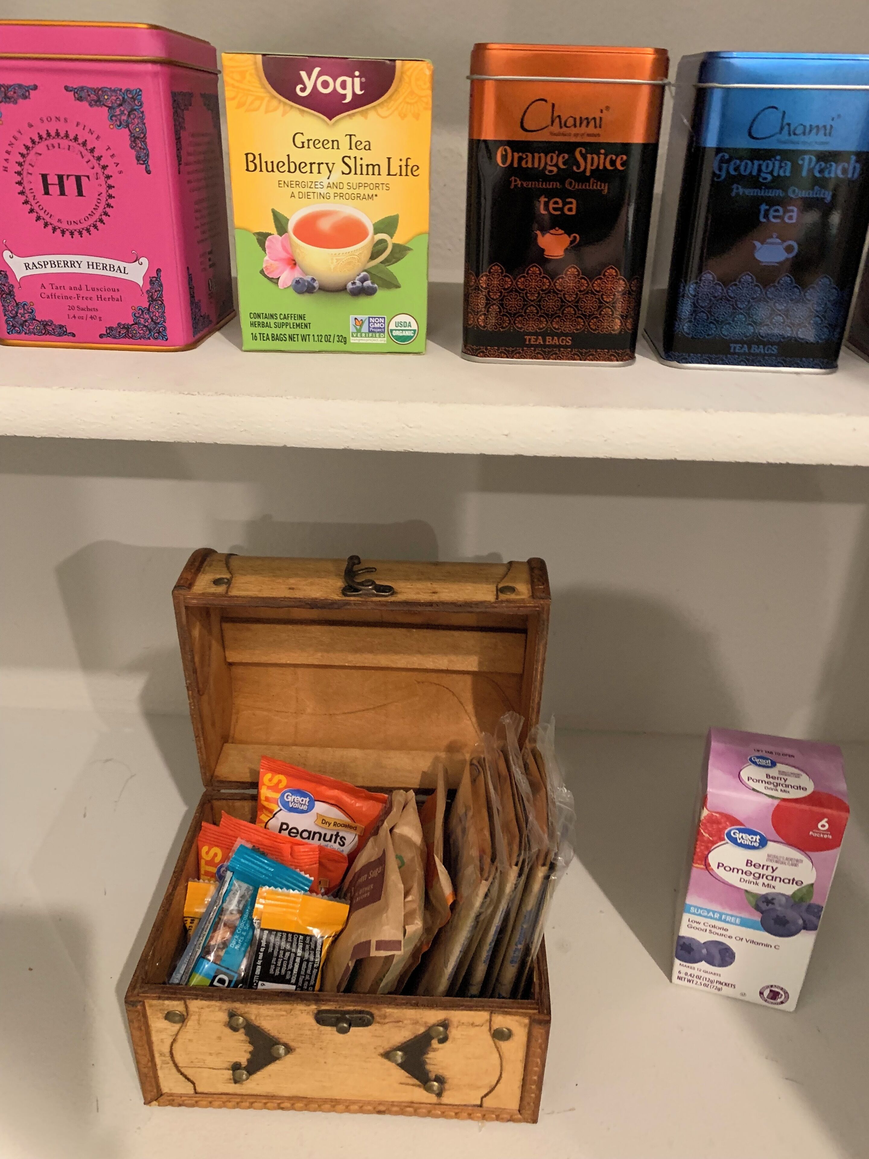 A shelf with tea tins and a wooden box containing various snacks and tea bags.