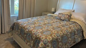 A bedroom with a patterned bedspread, a window with curtains, a nightstand, and a bedside lamp. -  New, clean, spacious and cozy! Pet friendly!  (Broken Arrow)