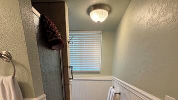 Un couloir étroit avec une douche, un porte-serviettes, un radiateur et une fenêtre avec des stores.