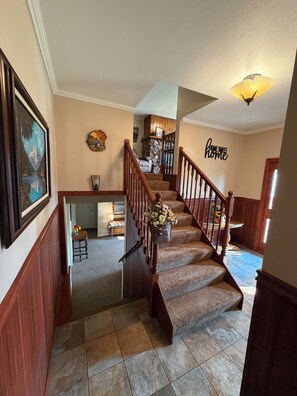 A staircase with wooden railings leading to a second floor, a stone fireplace, and a wall with a 'home sweet home' sign. - Wild Horse Retreat: Remodeled
Ranch House w/ River Views (Missoula)