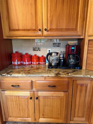 A kitchen with wooden cabinets, a granite countertop, and red kitchenware.