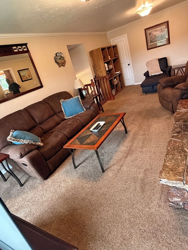 A living room with a brown sofa, a glass-top coffee table, and a bookshelf.