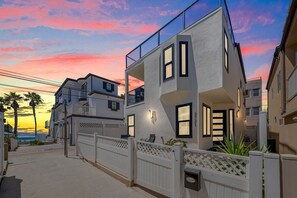 Ein modernes, zweistöckiges Gebäude mit Balkon, geschlossenem Eingang und Blick auf das Meer bei Sonnenuntergang.