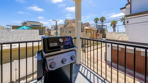 Un balcón con una parrilla Weber Spirit, vista a edificios residenciales y cielo despejado.