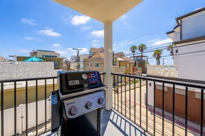 Ein Balkon mit einem Weber Spirit Grill, Blick auf Wohngebäude und einem klaren Himmel.