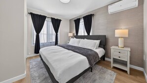 Un dormitorio moderno con una cama grande, mesitas de noche, una lámpara y un equipo de aire acondicionado.