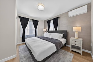 Ein modernes Schlafzimmer mit einem großen Bett, Nachttischen, einer Lampe und einer Klimaanlage.