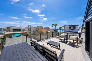Eine Dachterrasse mit Sitzgelegenheiten im Freien, einem Pool und Blick auf den Ozean sowie angrenzende Gebäude.