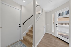 Ein Korridor mit Holzboden, einer weißen Tür und einer Treppe mit schwarzer Geländer.