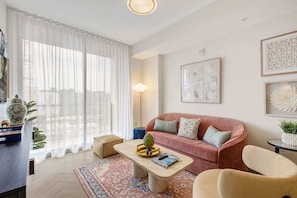 A modern living room with a sofa, coffee table, and chairs. There is a large window with sheer curtains, a floor lamp, and artwork on the walls. - Miami 1BR Apartment with Pool Ideal for 3 Guests (Miami)