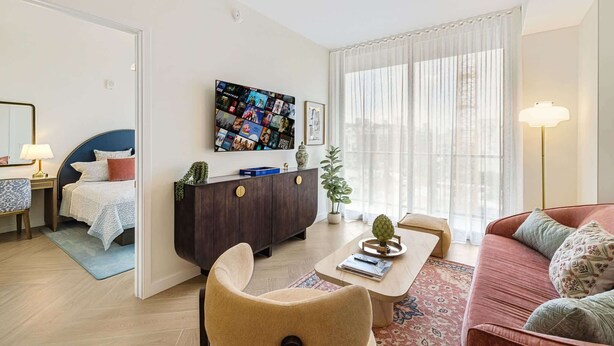 Ein modernes Wohnzimmer mit Sofa, Sessel, Couchtisch und einem an der Wand befestigten Fernseher.