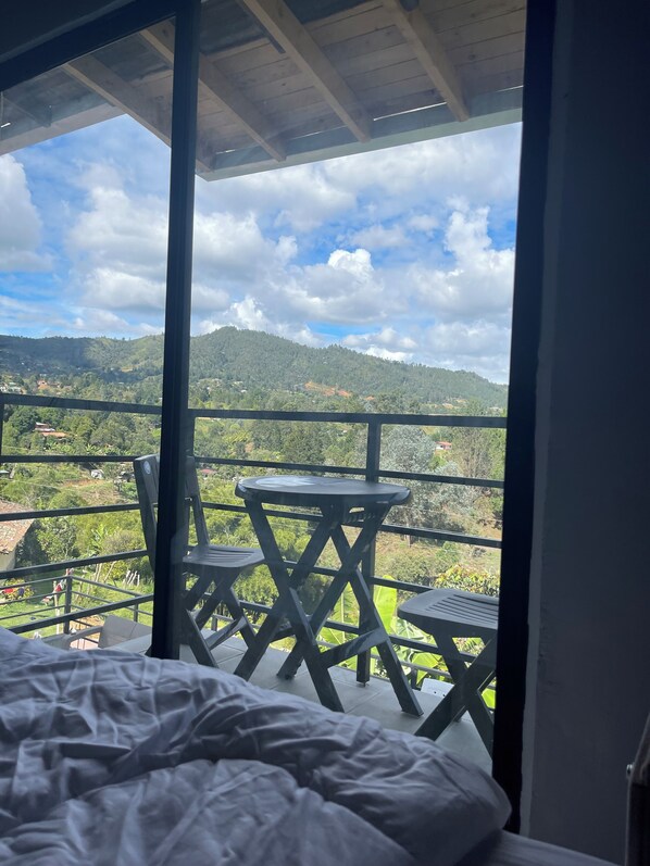 A bedroom with a large window overlooking a balcony with a table and chairs.