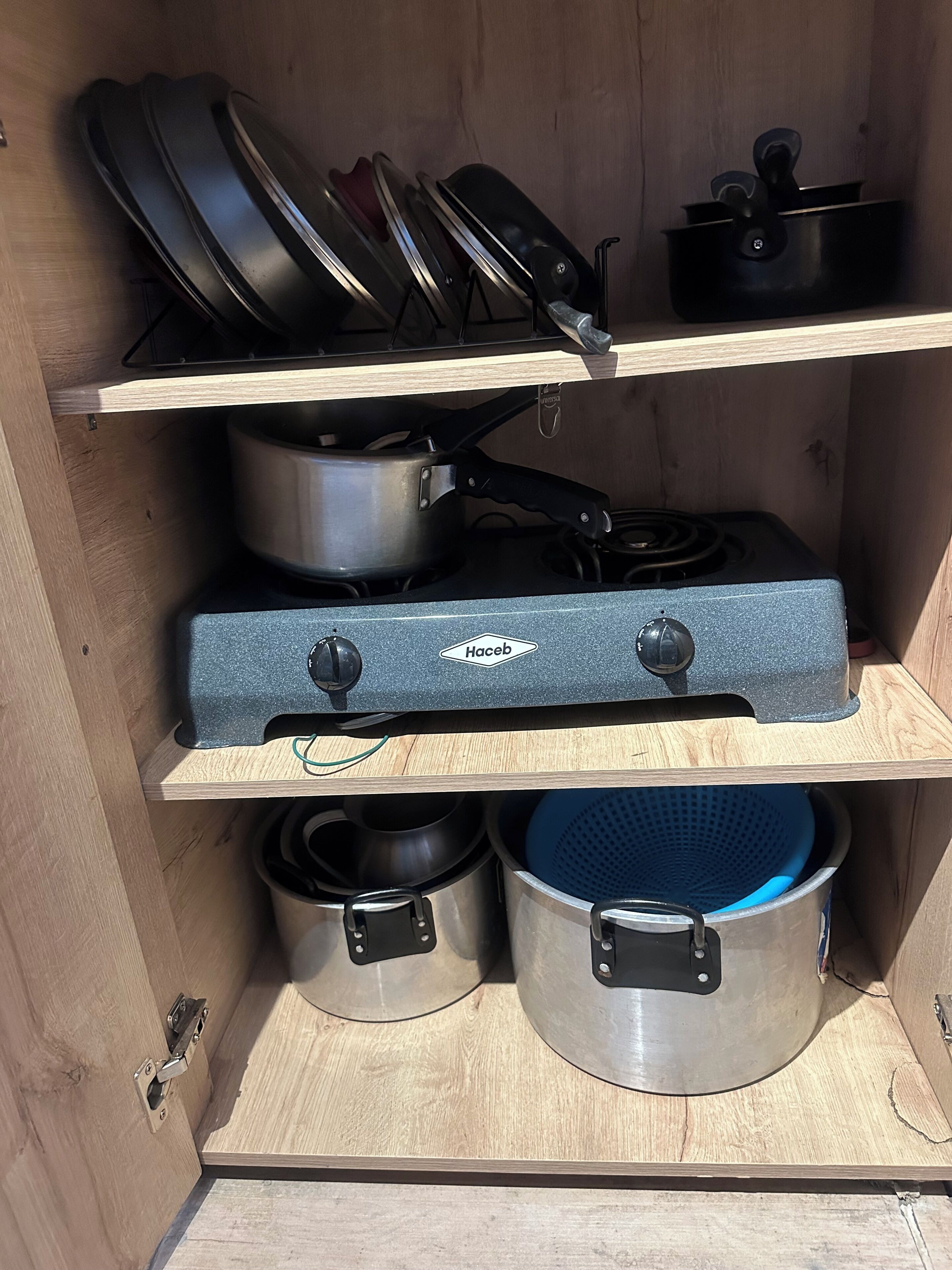 Ett köksskåp med hyllor för kokkärl, en spis och kastruller.