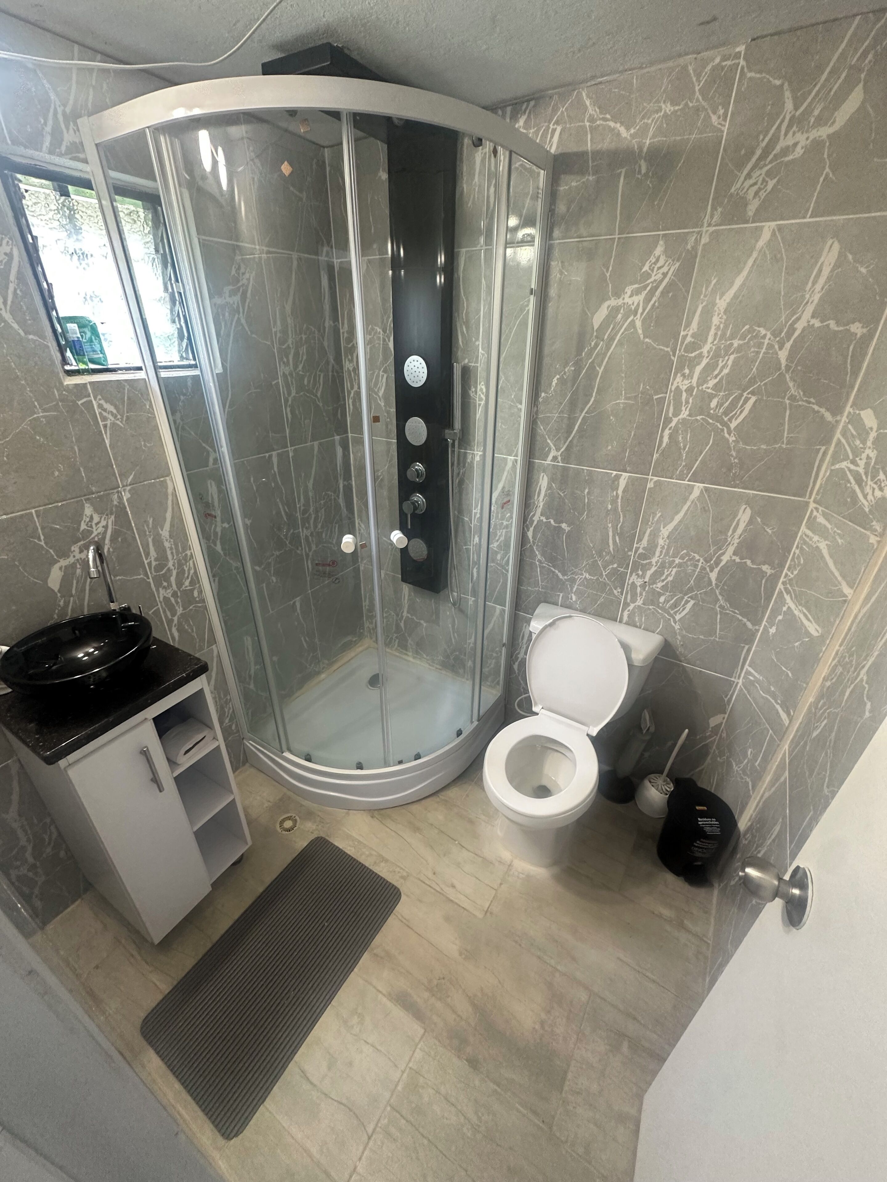 A bathroom with a curved shower enclosure, a toilet, a sink with a basin, and a small cabinet.