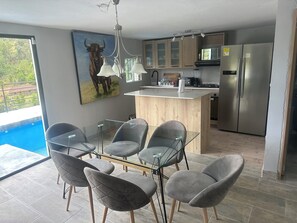 A modern kitchen with a central island, stainless steel appliances, and a dining area with glass-top tables and cushioned chairs.