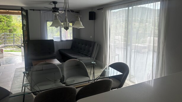 A modern living room with a glass dining table, two sofas, and a ceiling fan.