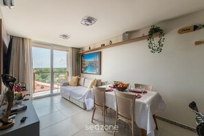 A modern living room with a dining area, large windows, and a view of the cityscape. - Apart in Condo w/ Pool and BBQ Aga0304 (Camaçari)
