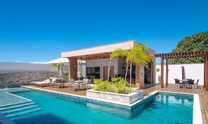 Ein Poolbereich mit überdachter Sitzecke, einem Pool und einer Pergola mit Pflanzen.