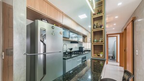 Uma cozinha moderna com geladeira embutida, fogão e micro-ondas. Há um armário de madeira acima do fogão e uma pequena prateleira com objetos decorativos.