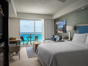 A hotel room with a large bed, a desk with a chair, a small table with a chair, and a view of the ocean through a sliding door. - Cancun Two Bedroom Villa Westin Lagunamar Resort (Cancún)