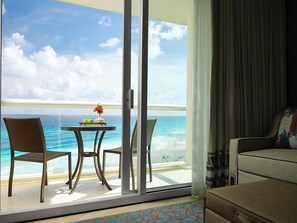 A room with a sliding glass door leading to a balcony overlooking a beach. There is a table with chairs and a small plant on the balcony. - Cancun Two Bedroom Villa Westin Lagunamar Resort (Cancún)
