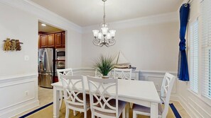 A dining area with a white table and chairs, a chandelier, and a view of the kitchen. - Bayside Resort - 36620 Day Lily Pkwy (Selbyville)
