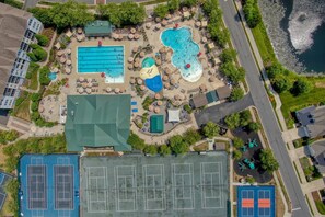 Luchtbeeld van een resort met verschillende zwembaden, tennisbanen en een strand.