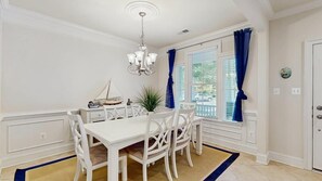 Ein Essbereich mit einem weißen Tisch und Stühlen, einer Kristallleuchter und einem Fenster mit blauen Vorhängen.