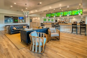 Un bar moderno con varias pantallas, una zona de estar con sofás y sillones, y piso de madera.