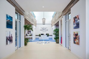 Un interior moderno con una mesa de recepción, un letrero que dice 'Welcome to the Health and Aquatic Club at Bayside' y una puerta de cristal que da a la zona de recepción.