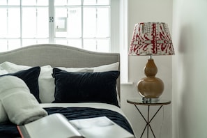 A bed with a grey headboard, white and navy blue bedding, and a bedside lamp with a patterned lampshade. - Welcome to your Stylish home in central London. (London)
