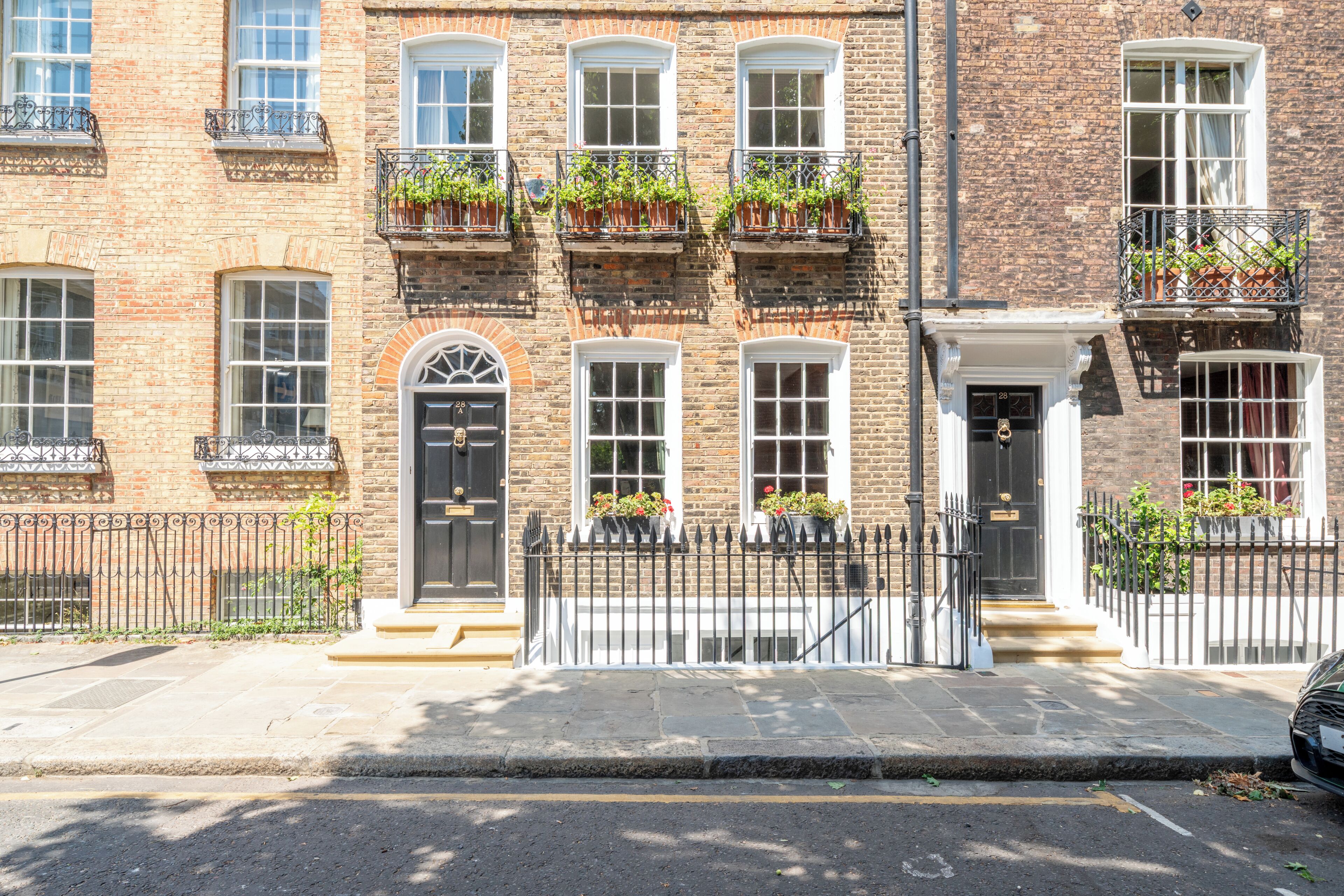 Rivissä on punatiilisistä rakennettuja kaupunkitaloja, joissa on useita ikkunoita, musta metalliaita ja parvekkeilla ruukkukasveja.
