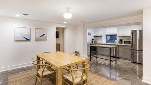 A modern kitchen with stainless steel appliances, a wooden dining table with chairs, and artwork on the wall. - Park House Garden - Ground Floor Two-Bedroom Apartment on Monterey Square (Savannah)