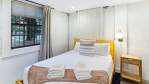 A hotel room with a bed, a nightstand, a lamp, and a window with curtains. - Park House Garden - Ground Floor Two-Bedroom Apartment on Monterey Square (Savannah)