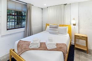 Ein Hotelzimmer mit Bett, Nachttisch, Lampe und einem Fenster mit Vorhängen.