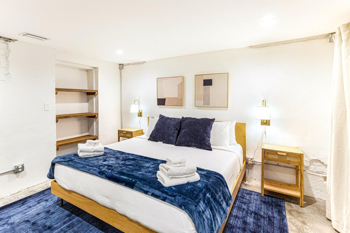 Une chambre d’hôtel avec un lit, deux tables de chevet, une étagère fixée au mur et une grande fenêtre.