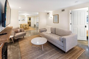 Ein modernes Wohnzimmer mit einer Couch, einem Couchtisch und einem Fernseher auf einem Holzständer.