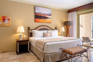 Habitación de hotel con una cama grande, dos mesitas de noche con lámparas, un banco, un cuadro en la pared y vistas al exterior a través de una ventana.