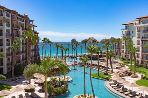 Un resort con varias piscinas, palmeras y vista al océano.