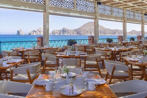 A seaside restaurant with tables set for dining, overlooking the ocean and mountains. - Luxury Resort with 1 bedroom and 2 bathrooms in gorgeous Cabo San Lucas (Cabo San Lucas)
