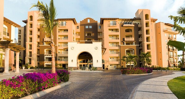 Un hotel de varios pisos con una entrada central, balcones y jardines circundantes.