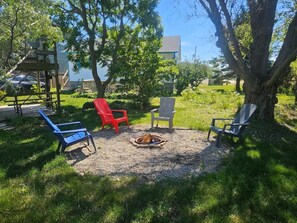 A backyard with a fire pit, four Adirondack chairs, and a wooden deck.