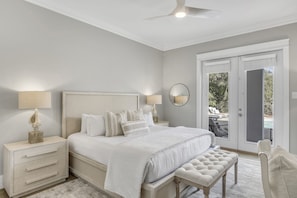 A bedroom with a large bed, two bedside tables with lamps, a round mirror, a bench, and a sliding glass door leading to an outdoor area. - Professionally Decorated with LSV and Pool (Seacrest Beach)