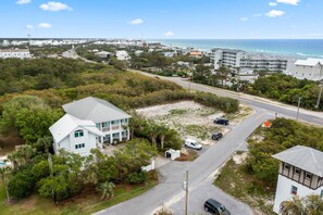 A coastal residential area with a prominent white house featuring a balcony, surrounded by lush greenery and a clear view of the ocean. - Professionally Decorated with LSV and Pool (Seacrest Beach)