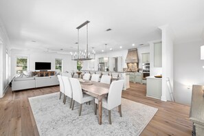 A spacious living room with a large white sofa, a dining area with a wooden table and white chairs, and a kitchen with white cabinets and a stone fireplace. - Professionally Decorated with LSV and Pool (Seacrest Beach)