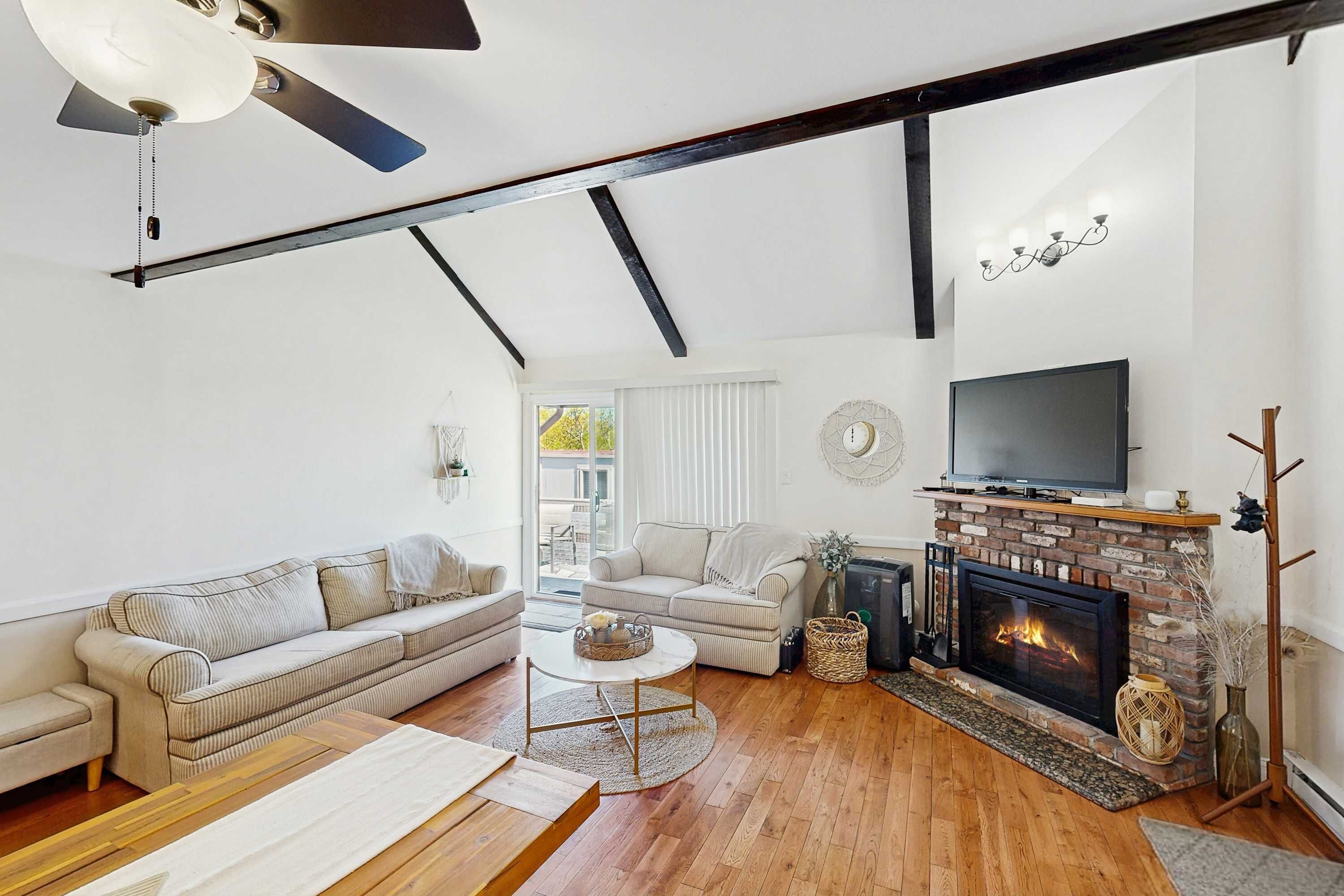 A modern living room with a fireplace, sofas, a TV, and a ceiling fan.