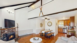 Un salón amplio con chimenea, televisor y comedor con mesa y bancos.