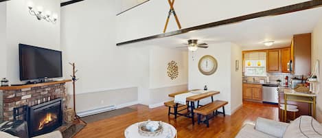 A spacious living room with a fireplace, a television, and a dining area with a table and benches.