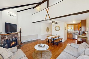 A spacious living room with a fireplace, a television, and a dining area with a table and benches. - Cozy 3BR Condo- Indoor Pool- Near Ski & Waterpark (Tannersville)