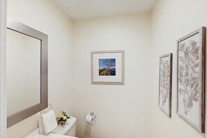 Ein Badezimmer mit Toilette, Handtuchhalter, einem gerahmten Bild und Toilettenpapierhalter.